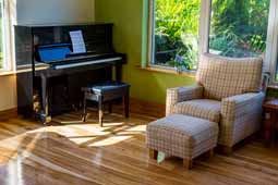 Black piano, sitting room armchair ( red and white pattern ) with matching footstool on Ash Hard Wood Floor