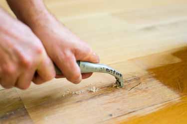 Workman's hands using hand scraper to scrape varnish from wood floor