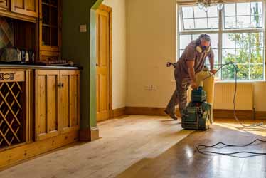 Floor Sanding in progress - Image of work man carrying out wood floor sanding in kitchen