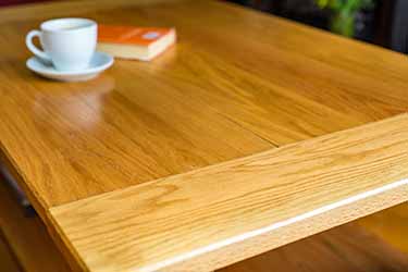 image of sanded and varnished oak wood table with white cup and saucer and orange hard backed book on top 